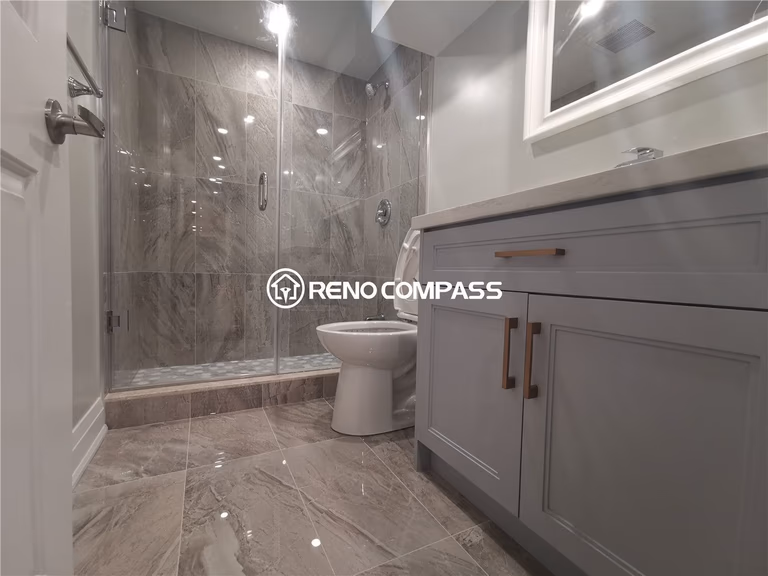 This Markham basement renovation showcases a fully upgraded bathroom featuring a glass-enclosed walk-in shower, marble-look porcelain tiles, modern vanity with quartz countertop, and sleek chrome fixtures. The combination of large-format floor tiles and detailed shower mosaic flooring enhances durability, water resistance, and visual appeal. A clean neutral color palette and contemporary finishes create a bright and functional basement bathroom environment. Completed by a professional Toronto renovation company, this project highlights expert tile installation, quality plumbing fixtures, and modern basement bathroom design tailored for homes in the Greater Toronto Area.