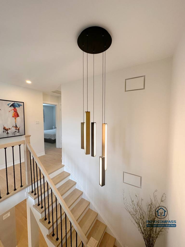 This Toronto stair renovation features custom hardwood steps, black metal railings, and modern pendant lighting that enhances vertical space and architectural depth. The seamless integration of stair design and flooring creates a bright, cohesive interior, showcasing refined craftsmanship ideal for contemporary Toronto home renovations.