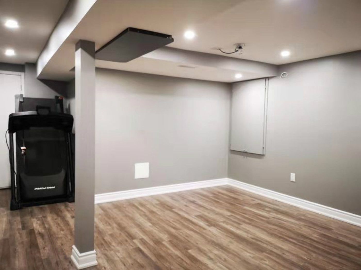 This completed Mississauga basement renovation showcases a clean open space with modern vinyl flooring, recessed pot lights, and a structural support column seamlessly integrated into the design. The upgraded layout offers flexibility for living or fitness use, highlighting the quality work of a professional Toronto renovation company.