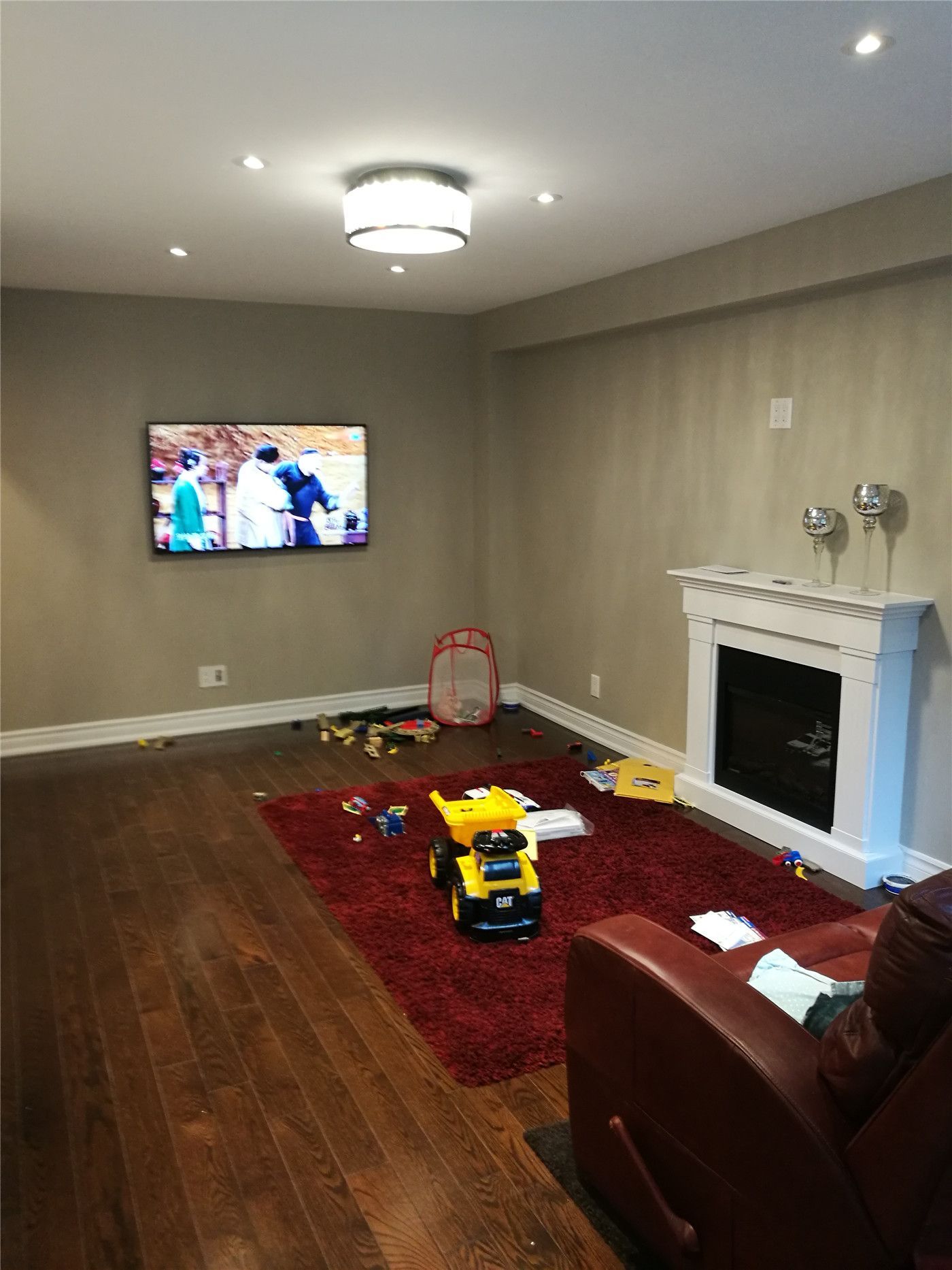 This Newmarket interior renovation features a refreshed family room with dark hardwood flooring, recessed ceiling lights, and a modern flush-mount light fixture. A clean fireplace surround and wall-mounted TV create a comfortable and functional living space, showcasing the quality craftsmanship of a professional Toronto renovation company.