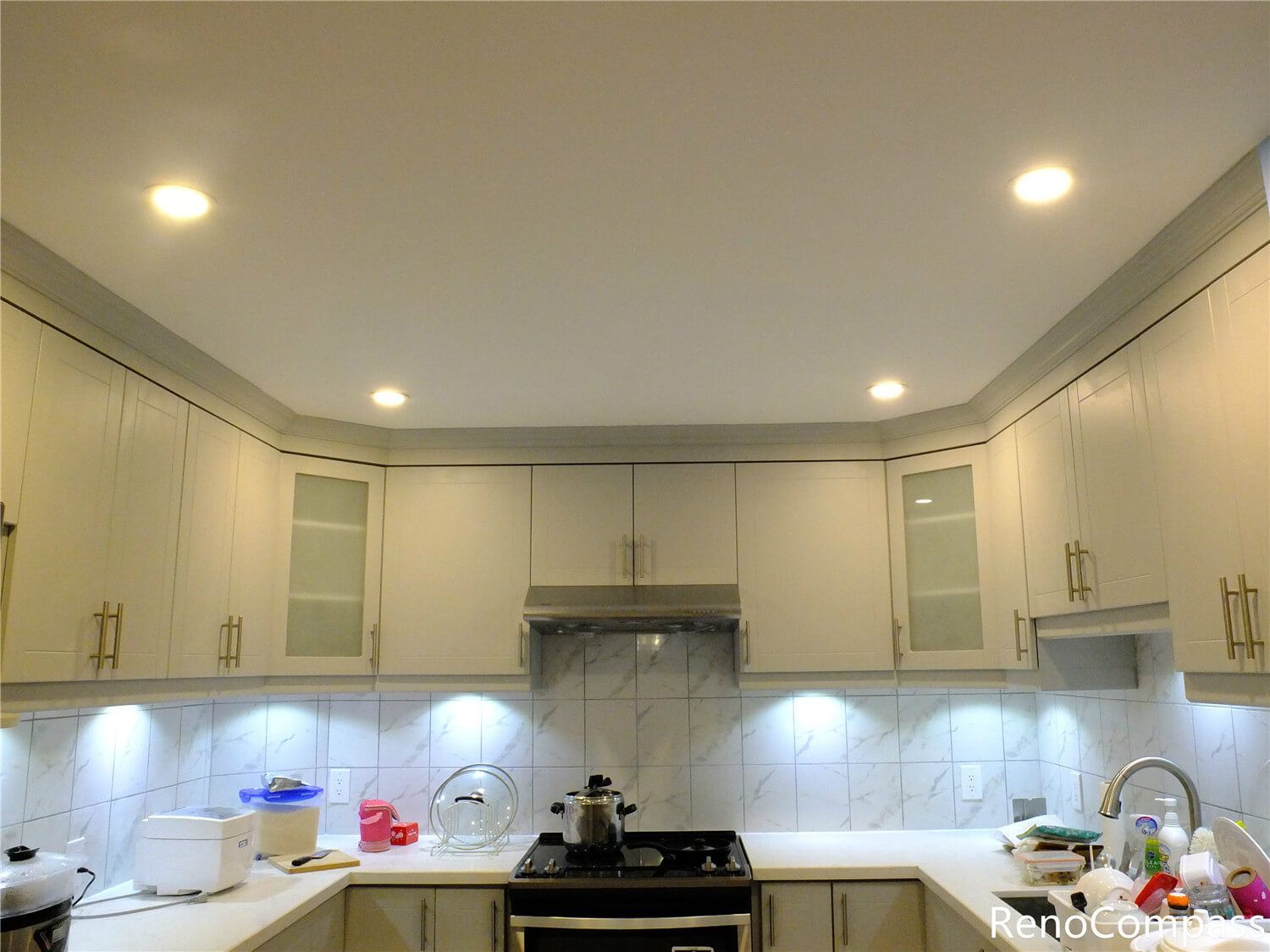This Aurora kitchen renovation features elegant custom white cabinetry with gold hardware, a marble-style backsplash, and modern recessed lighting. The upgraded layout improves functionality while creating a bright and sophisticated cooking space. Completed with clean countertop finishes and integrated under-cabinet lighting, this renovation reflects the quality craftsmanship and attention to detail delivered by Reno Compass Inc., a trusted Toronto renovation company serving Aurora and the Greater Toronto Area.