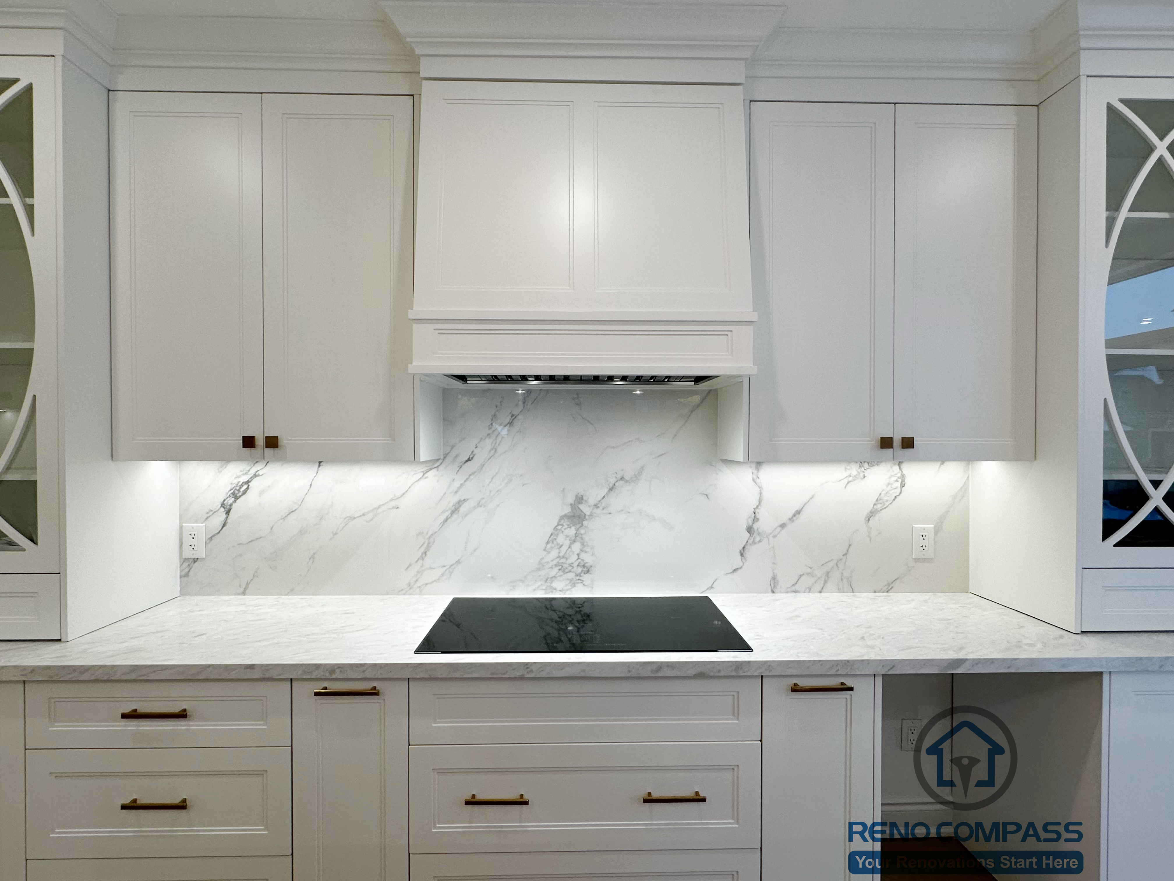 Detailed view of custom kitchen cabinetry completed as part of a Vaughan interior renovation, featuring shaker-style white cabinets, marble-look backsplash, under-cabinet lighting, quartz countertops, and a built-in cooktop. The refined finishes and precise detailing highlight the craftsmanship of a professional Toronto renovation company.