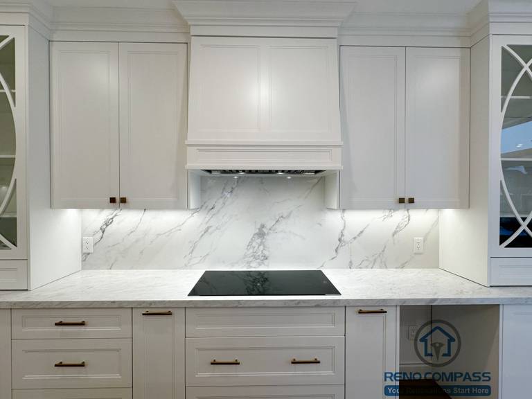 Detailed view of custom kitchen cabinetry completed as part of a Vaughan interior renovation, featuring shaker-style white cabinets, marble-look backsplash, under-cabinet lighting, quartz countertops, and a built-in cooktop. The refined finishes and precise detailing highlight the craftsmanship of a professional Toronto renovation company.