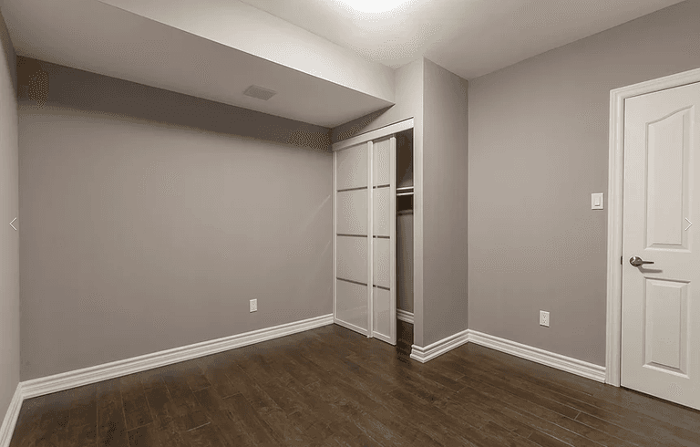 This Toronto basement renovation includes a newly finished bedroom featuring engineered hardwood flooring, smooth ceilings, recessed lighting, and a modern sliding glass closet door system. The neutral wall color enhances brightness while maximizing usable space. Professionally designed and completed by Reno Compass Inc., a trusted Toronto renovation company specializing in basement finishing and interior remodeling.