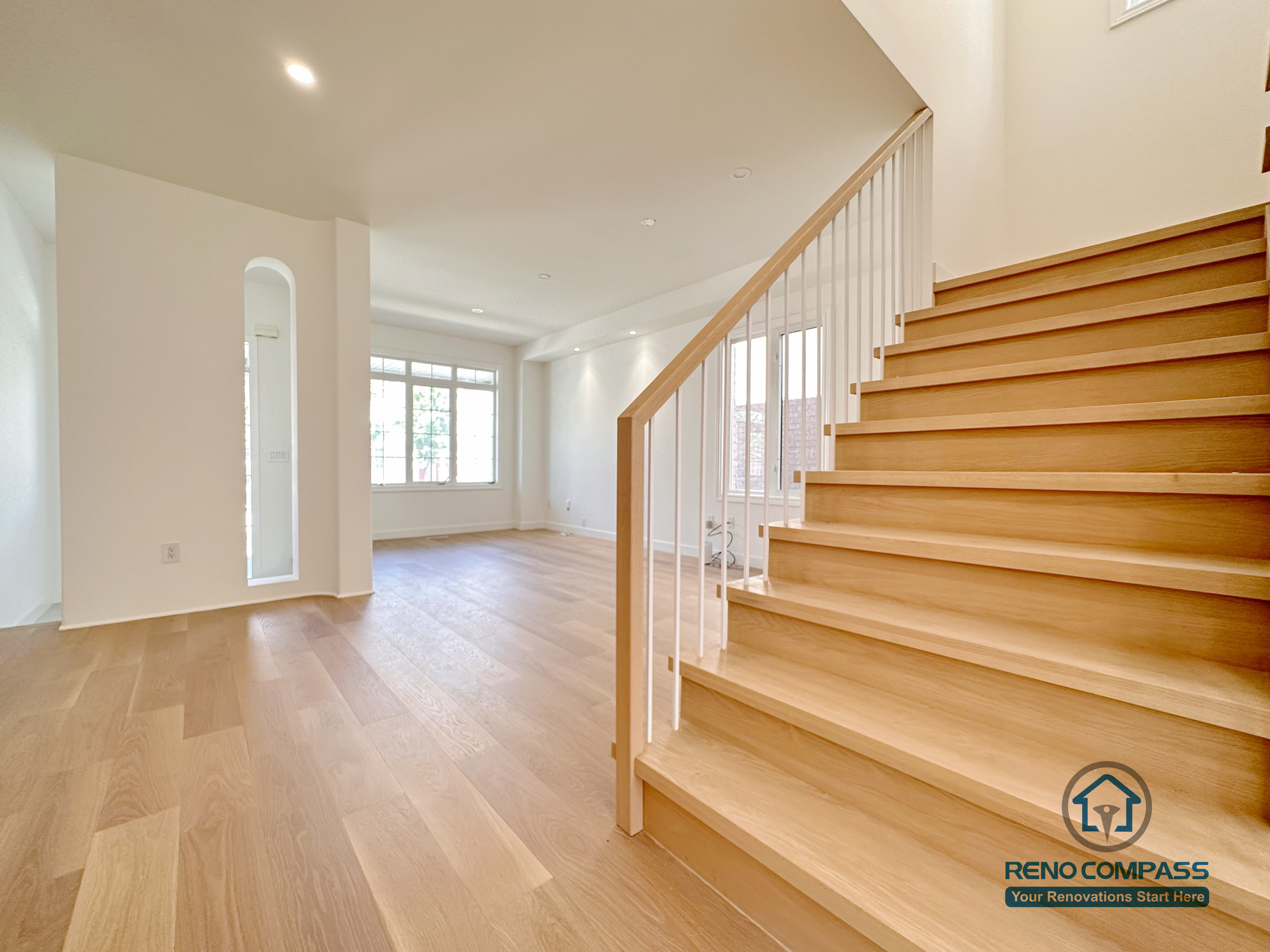 This image showcases a Markham flooring and stair renovation featuring wide-plank hardwood flooring and an open staircase with natural wood treads and white vertical railings. The seamless connection between the staircase and main living area enhances openness, light flow, and spatial continuity. Completed by a professional Toronto renovation company, Reno Compass Inc., the design balances modern simplicity with long-term durability.