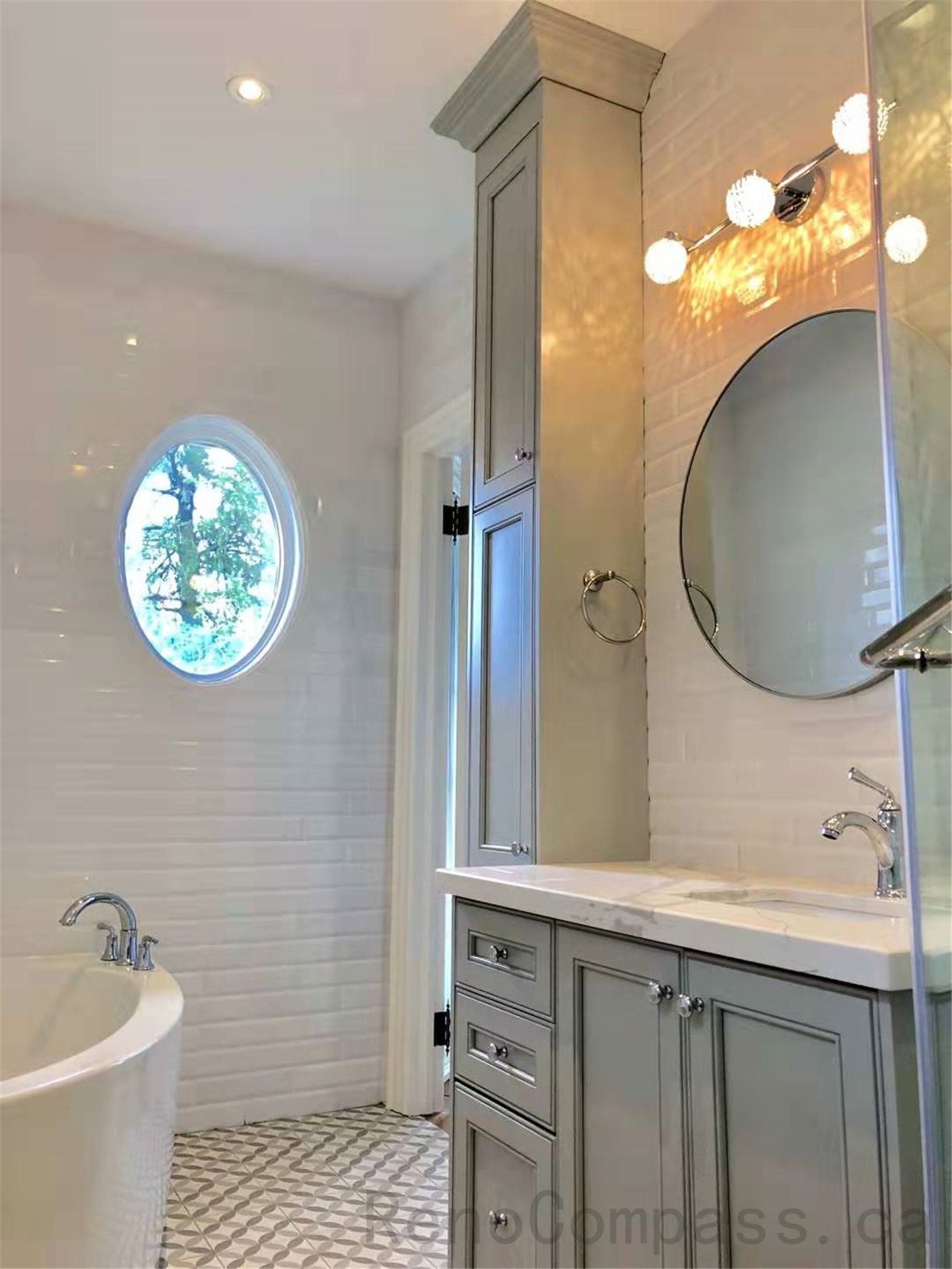 This North York bathroom renovation features a freestanding bathtub paired with custom vanity cabinetry, integrated storage, and a round window that brings in natural light. Neutral finishes, classic tilework, and layered lighting create a calm and elegant bathroom environment designed for daily comfort and relaxation.