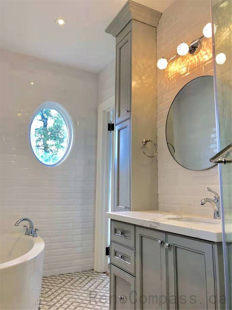 This North York bathroom renovation features a freestanding bathtub paired with custom vanity cabinetry, integrated storage, and a round window that brings in natural light. Neutral finishes, classic tilework, and layered lighting create a calm and elegant bathroom environment designed for daily comfort and relaxation.
