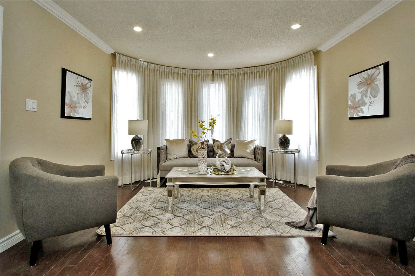 This Toronto interior design pre-sale staging project features a bright living room with a curved bay window, sheer curtains, modern neutral-toned furniture, and elegant decor. The professionally styled space enhances natural light, highlights spacious layout, and creates a warm, inviting atmosphere for potential buyers.