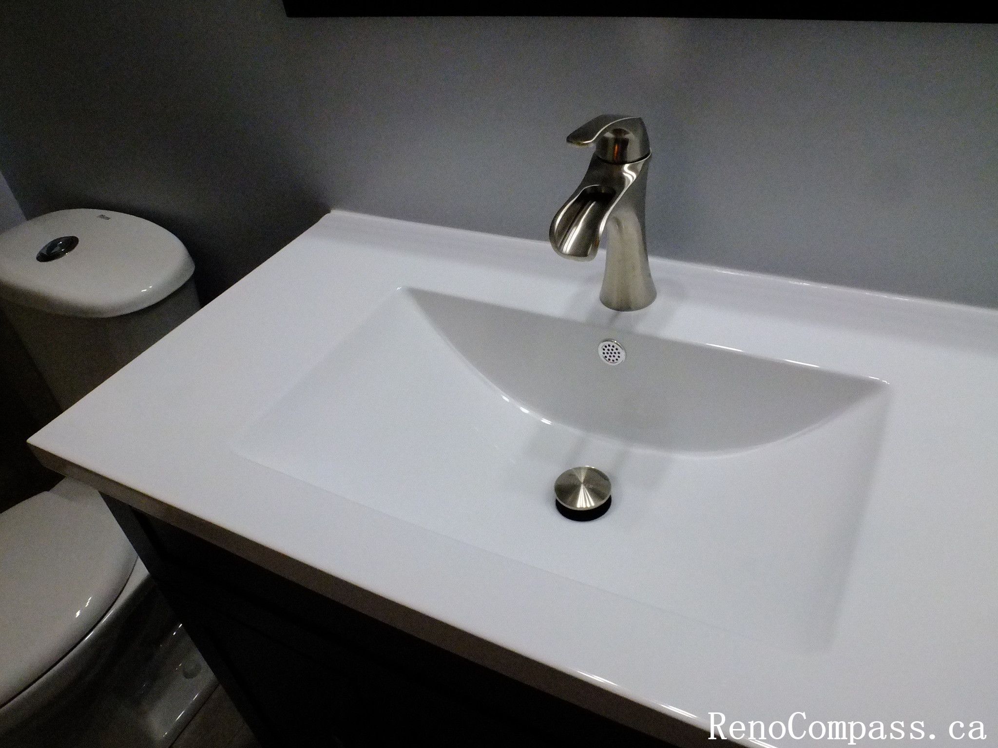 Modern bathroom vanity installed during a Richmond Hill interior renovation project. The design features a sleek white integrated sink, brushed nickel faucet, and dark vanity cabinet that contrasts beautifully with the neutral wall finish. This upgrade enhances both functionality and visual appeal in the bathroom. Completed by Reno Compass Inc., a trusted Toronto renovation company specializing in bathroom and interior renovations.