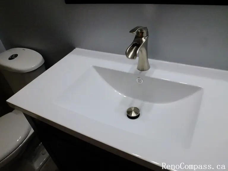 Modern bathroom vanity installed during a Richmond Hill interior renovation project. The design features a sleek white integrated sink, brushed nickel faucet, and dark vanity cabinet that contrasts beautifully with the neutral wall finish. This upgrade enhances both functionality and visual appeal in the bathroom. Completed by Reno Compass Inc., a trusted Toronto renovation company specializing in bathroom and interior renovations.