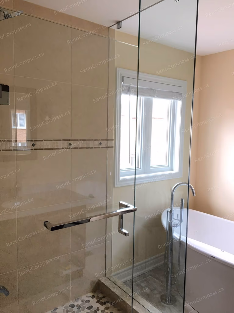 This Markham interior renovation features a modern bathroom upgrade with a frameless glass shower enclosure, elegant tile work, and a sleek freestanding bathtub. Natural light from the window enhances the warm and relaxing atmosphere, creating a spa-like bathing space. Completed by Reno Compass, a trusted Toronto renovation company specializing in high-quality bathroom and interior renovations.