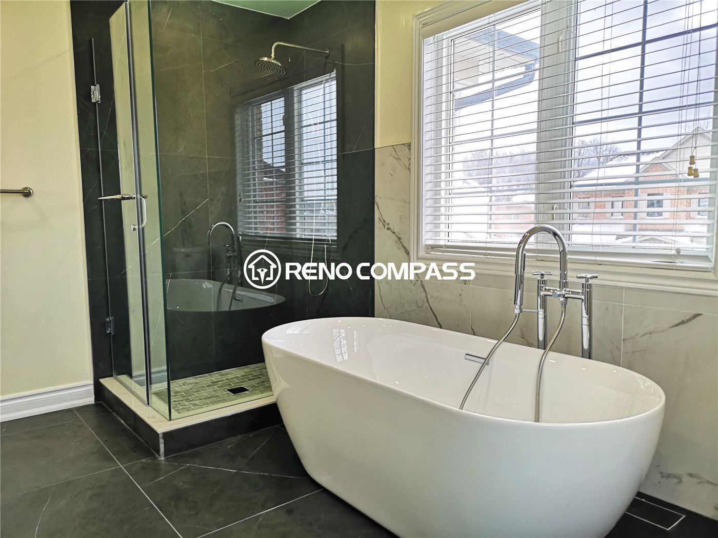 This stylish Toronto bathroom renovation features a sleek freestanding bathtub beside a frameless glass shower. Elegant marble and dark tile flooring create a modern and luxurious spa-like atmosphere. Designed and completed by Reno Compass for a high-end contemporary home upgrade.