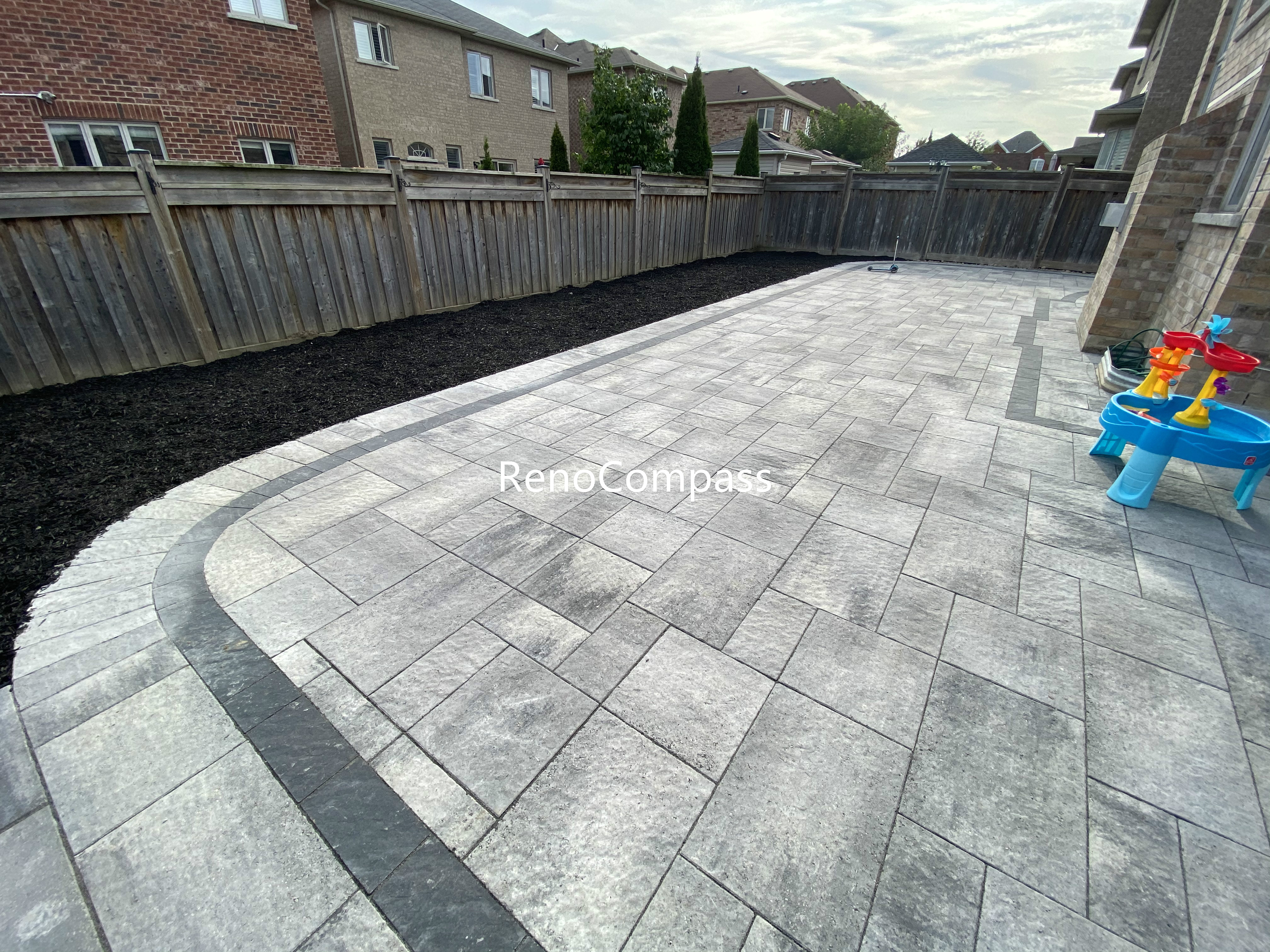 This Aurora backyard interlocking paver patio features a spacious layout with a curved border design that adds visual flow and architectural interest. Large-format concrete pavers are arranged in a clean, linear pattern, while the contrasting border enhances structure and edge definition. The durable interlock surface provides excellent drainage, stability, and low maintenance, making it ideal for daily use and outdoor activities. This professionally completed backyard paving project improves both functionality and aesthetics, offering a modern outdoor living space for residential properties in Aurora.