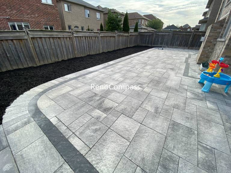This Aurora backyard interlocking paver patio features a spacious layout with a curved border design that adds visual flow and architectural interest. Large-format concrete pavers are arranged in a clean, linear pattern, while the contrasting border enhances structure and edge definition. The durable interlock surface provides excellent drainage, stability, and low maintenance, making it ideal for daily use and outdoor activities. This professionally completed backyard paving project improves both functionality and aesthetics, offering a modern outdoor living space for residential properties in Aurora.