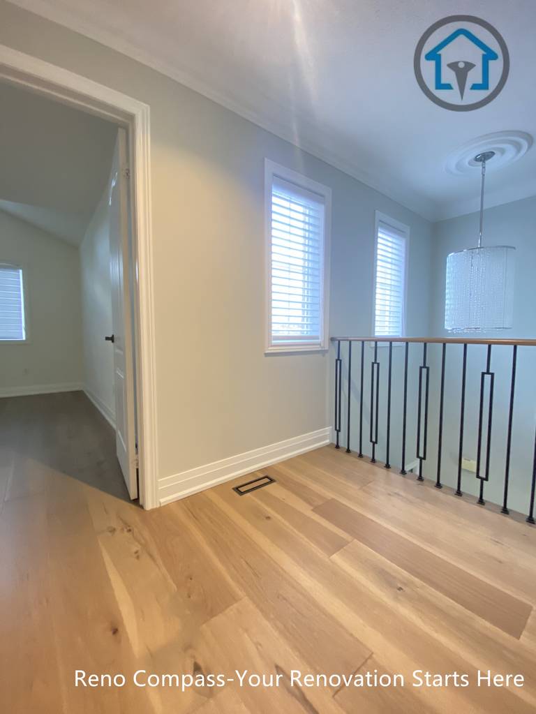 This image shows the upper hallway and stair landing area of a flooring and staircase renovation project in Richmond Hill. The space features continuous hardwood flooring, clean wall finishes, and modern black iron railings that create a safe yet visually open transition between rooms and levels. Natural light from multiple windows enhances the brightness and depth of the hallway. Completed by a reliable Toronto renovation company, the renovation emphasizes smooth circulation, durable materials, and a cohesive modern interior design.
