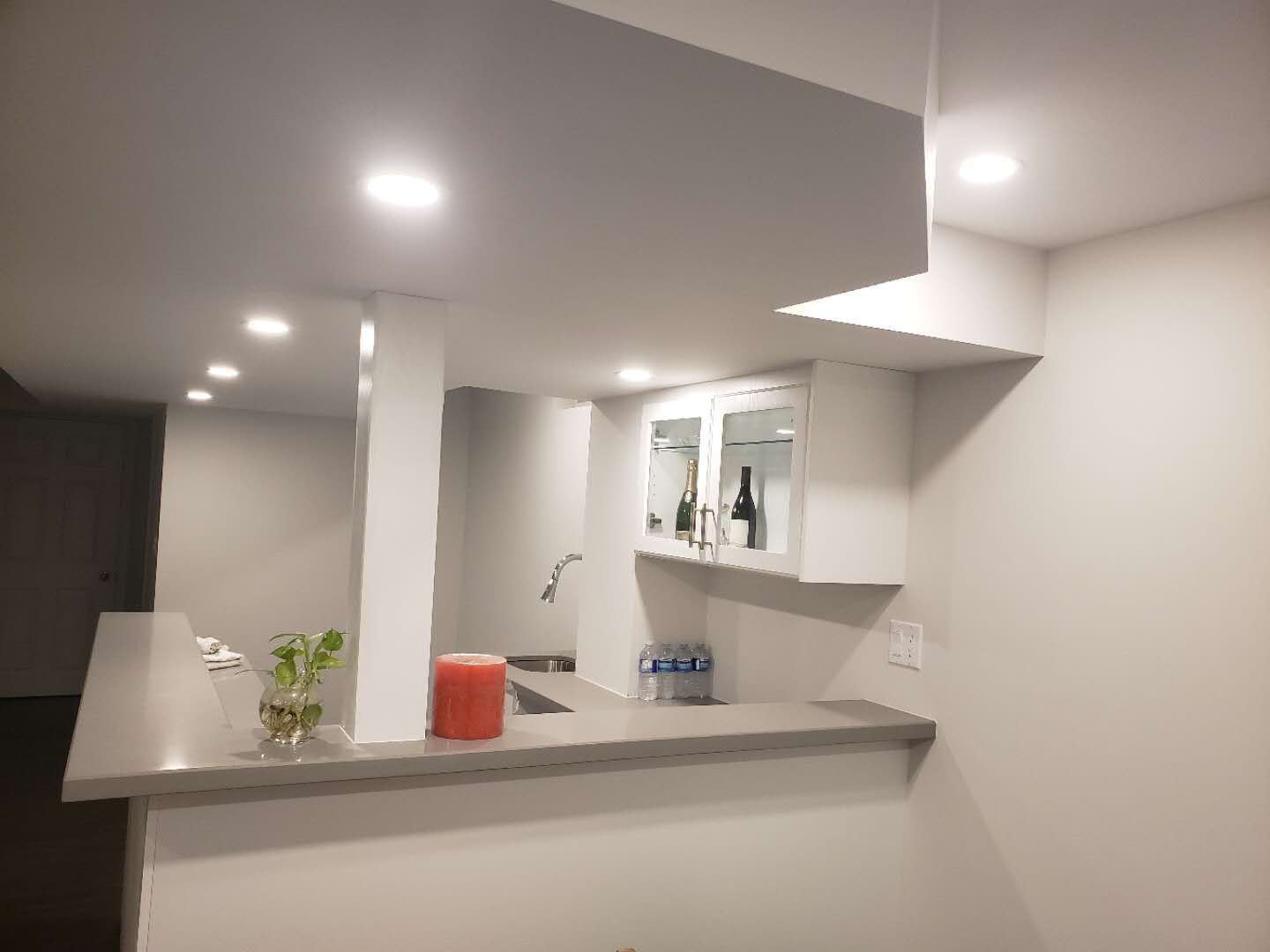 This Markham basement renovation showcases a modern custom bar and countertop area designed for both functionality and style. The space features sleek white cabinetry, a built-in sink, wall-mounted storage, and a spacious serving counter ideal for entertaining. Recessed pot lights provide even illumination across the basement, enhancing the clean ceiling design and open layout. Neutral wall tones paired with durable flooring create a warm and contemporary atmosphere. This professionally renovated basement in Markham highlights practical design, efficient use of space, and quality craftsmanship suitable for modern family living.
