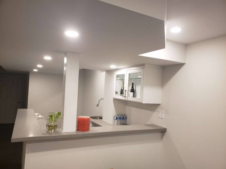 This Markham basement renovation showcases a modern custom bar and countertop area designed for both functionality and style. The space features sleek white cabinetry, a built-in sink, wall-mounted storage, and a spacious serving counter ideal for entertaining. Recessed pot lights provide even illumination across the basement, enhancing the clean ceiling design and open layout. Neutral wall tones paired with durable flooring create a warm and contemporary atmosphere. This professionally renovated basement in Markham highlights practical design, efficient use of space, and quality craftsmanship suitable for modern family living.