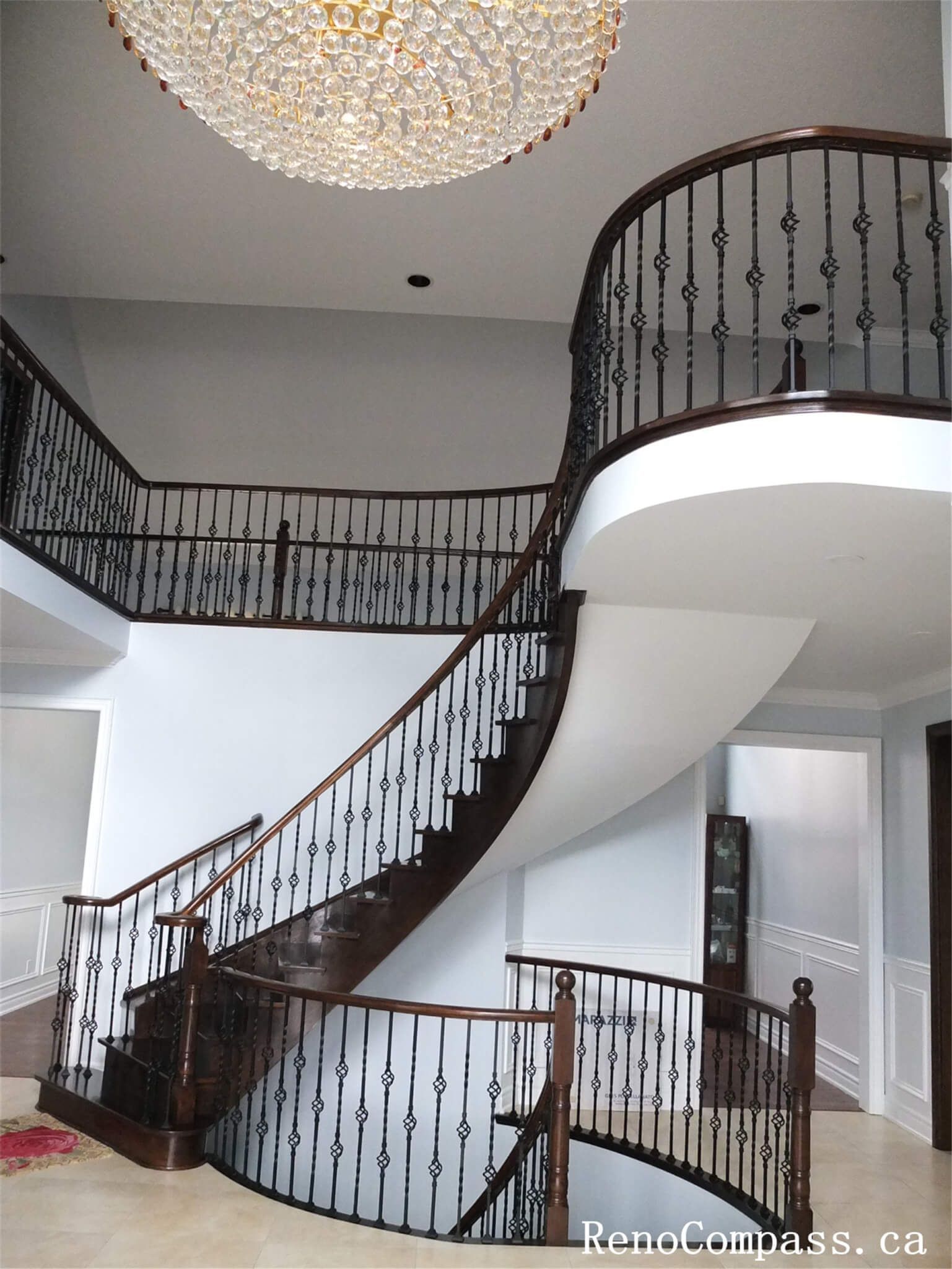 This Richmond Hill interior renovation features an elegant curved staircase with dark wood steps and custom wrought iron railings. The staircase repainting and refinishing enhance the home's architectural beauty while creating a refined transition between floors.
