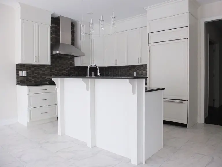 This Kleinburg interior renovation features a bright and elegant modern kitchen with custom white cabinetry, marble-style flooring, and a functional island with built-in sink. The design combines clean lines, stainless steel appliances, and a dark mosaic backsplash to create a refined contrast while maintaining a spacious and contemporary feel. The kitchen island also provides additional workspace and seating, making the space both stylish and highly practical for everyday living.