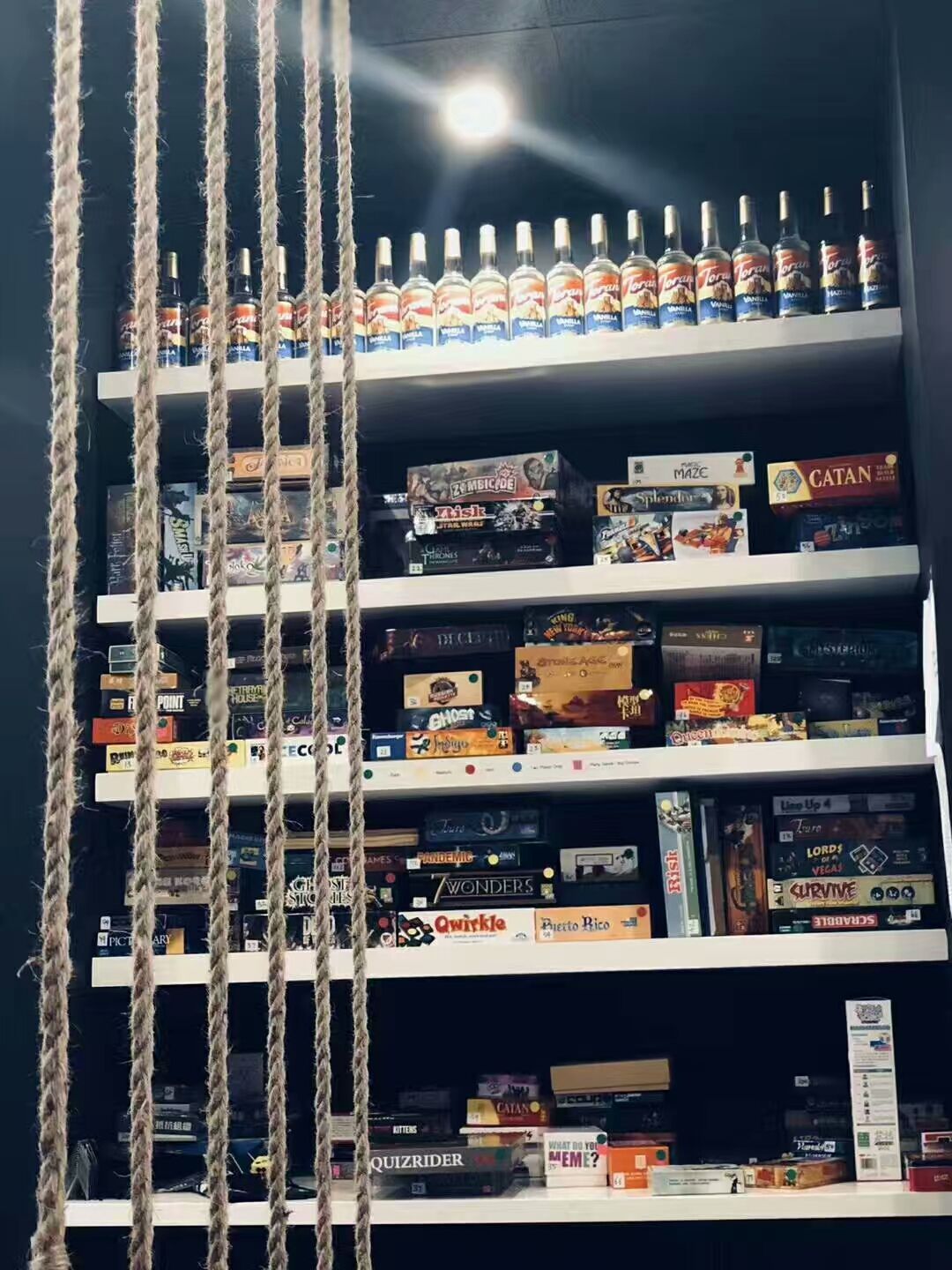 This image features custom display shelving installed in a bubble tea shop commercial renovation project in Scarborough. The shelving unit is used to organize board games and beverage displays, creating an interactive and welcoming environment for customers. Combined with decorative rope dividers and modern lighting, the space blends functionality with creative interior design. The renovation enhances the customer experience by offering a comfortable social area within the bubble tea shop.