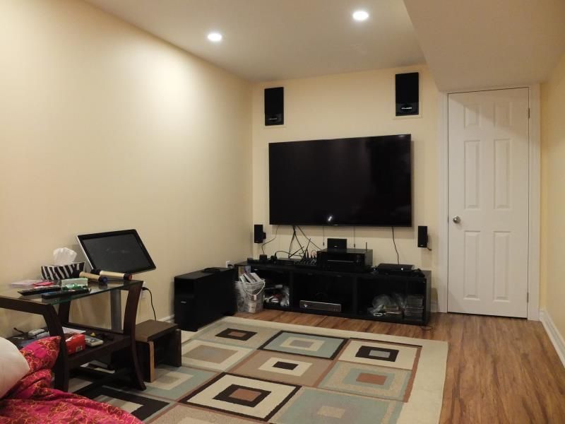A renovated basement in Vaughan featuring a comfortable home‑theatre area with a wall‑mounted TV, built‑in speakers, entertainment console, warm lighting, and wood‑style flooring. A functional and inviting space designed for relaxation and family entertainment.