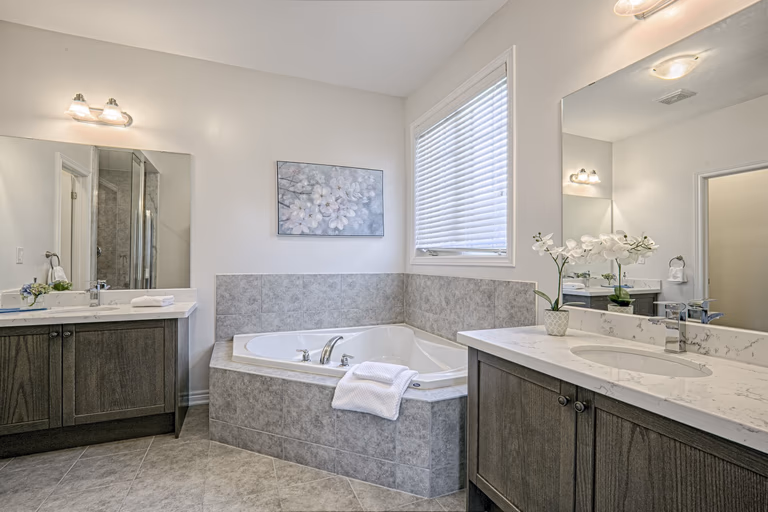 This Toronto luxury master bathroom renovation features a spacious layout with a double vanity, premium stone countertops, and a built-in soaking tub surrounded by elegant tile finishes. The design includes modern lighting, large mirrors, and neutral tones that create a bright and relaxing spa-like environment. Completed by a professional Toronto renovation company, this bathroom project showcases high-quality craftsmanship, functional layout planning, and contemporary residential design tailored for modern comfort.