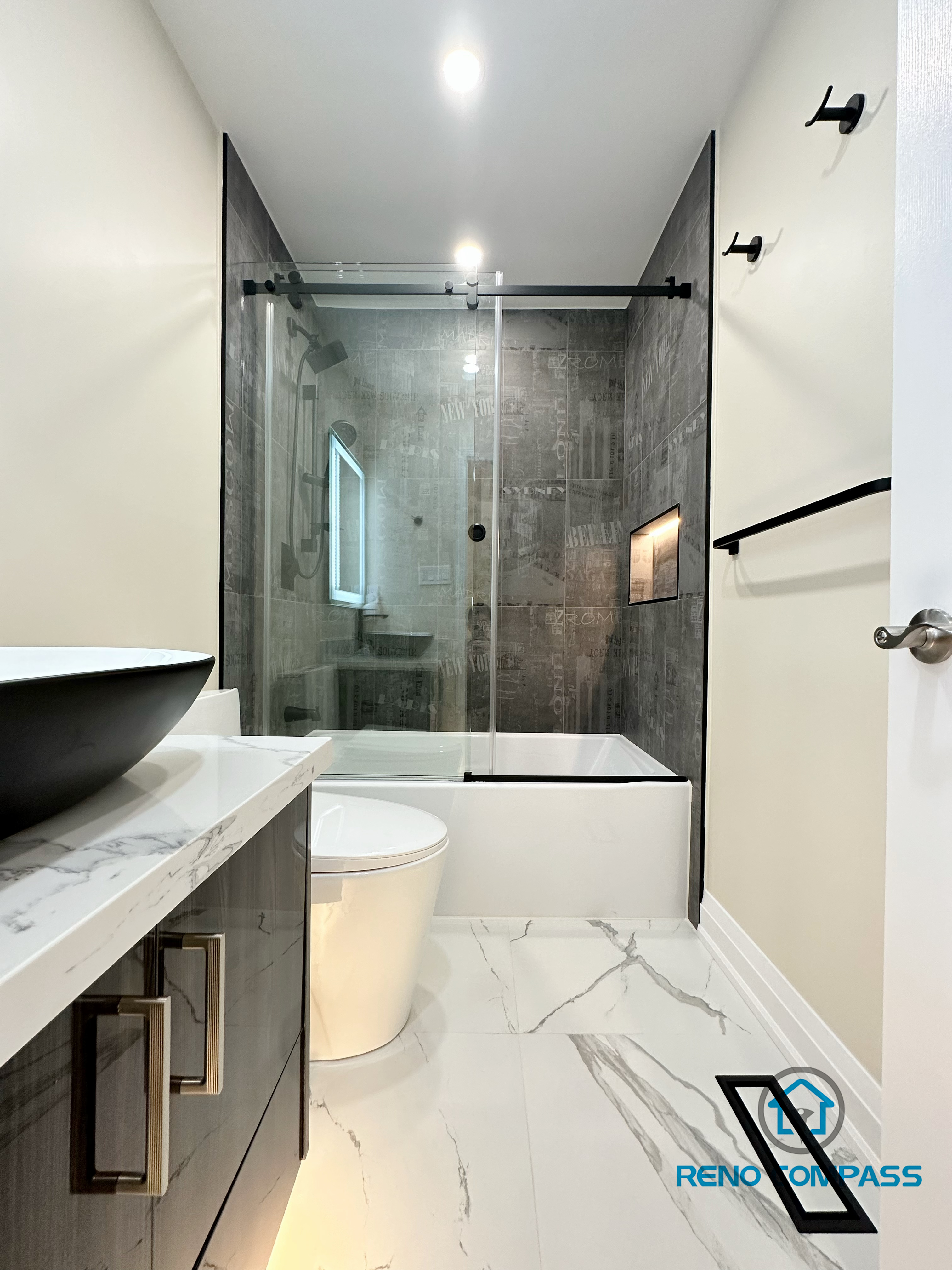 Modern bathroom renovation in Vaughan presenting a full layout view with a sleek vanity, vessel sink, and quartz countertop in the foreground, paired with a frameless glass shower enclosure and integrated wall niche in the background. Marble-look porcelain floor tiles and large-format shower wall tiles create a clean and cohesive design. This thoughtfully planned space highlights efficient layout, refined finishes, and quality craftsmanship delivered by a professional Toronto renovation company.