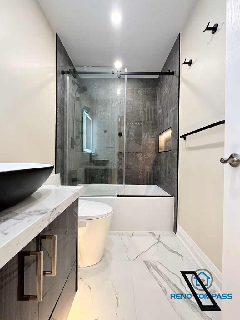 Modern bathroom renovation in Vaughan presenting a full layout view with a sleek vanity, vessel sink, and quartz countertop in the foreground, paired with a frameless glass shower enclosure and integrated wall niche in the background. Marble-look porcelain floor tiles and large-format shower wall tiles create a clean and cohesive design. This thoughtfully planned space highlights efficient layout, refined finishes, and quality craftsmanship delivered by a professional Toronto renovation company.