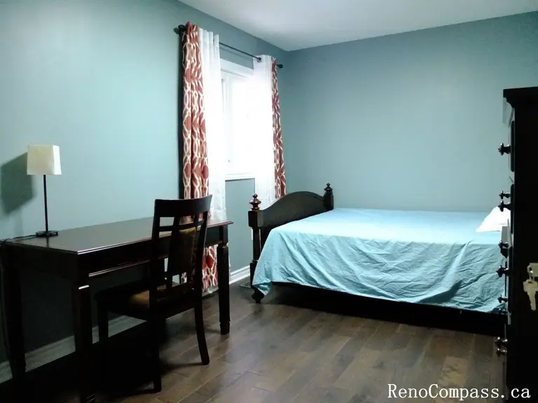 This Richmond Hill interior renovation showcases a bright and practical bedroom featuring hardwood flooring, natural light from large windows, and a functional furniture layout. The space includes a workspace area and storage solutions, creating a comfortable and well-organized environment. Completed by a Toronto renovation company, this design emphasizes simplicity, usability, and modern living.