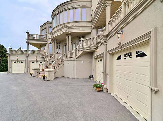 Detailed exterior view of a luxury custom house rebuild in Toronto featuring elegant curved architecture, grand stone staircase, decorative columns, and multiple garage entrances. This large-scale residential renovation highlights refined exterior craftsmanship and architectural design completed by Reno Compass, a professional Toronto Renovation Company specializing in luxury home rebuilds, custom homes, and full interior renovations across the GTA.