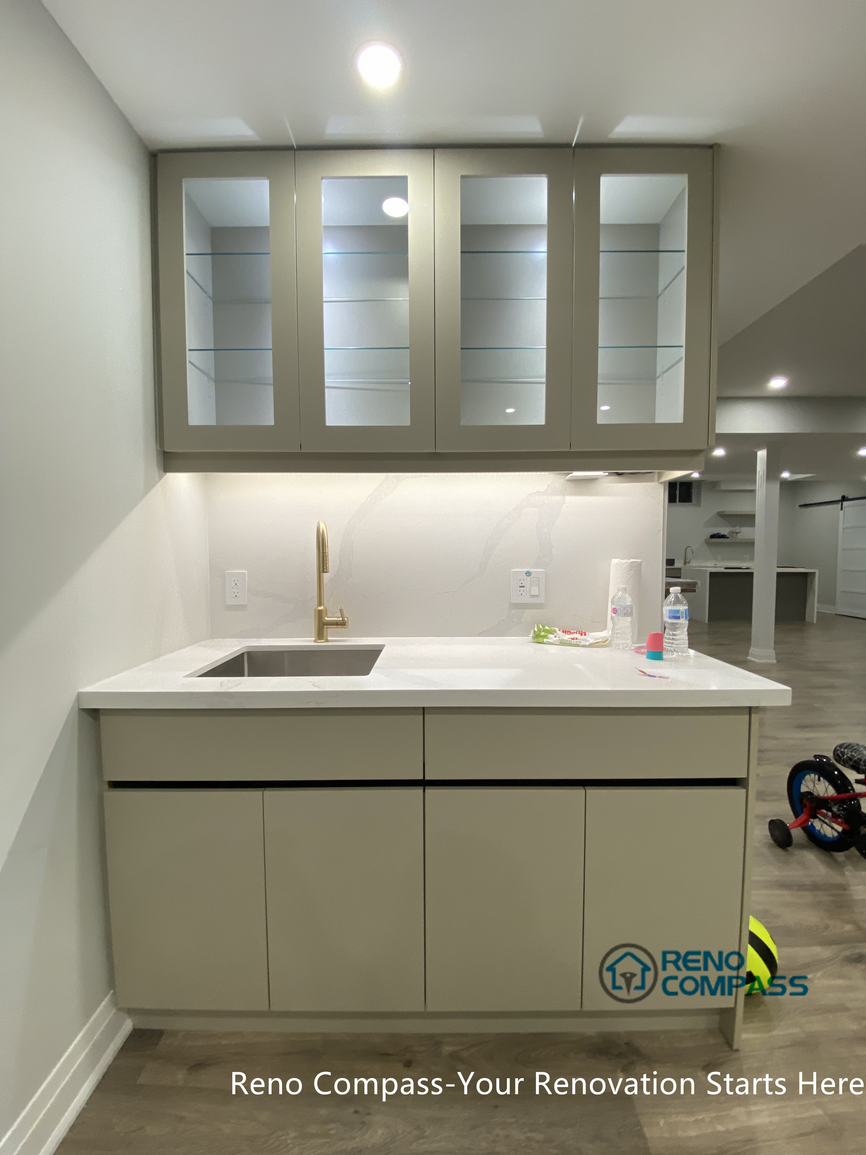This Newmarket basement renovation highlights a custom wet bar cabinet with glass-front upper storage, quartz countertop, and a sleek integrated sink. Completed by a professional Toronto renovation company, the design combines clean lines, functional storage, and refined finishes, enhancing both usability and visual appeal within a modern finished basement setting.