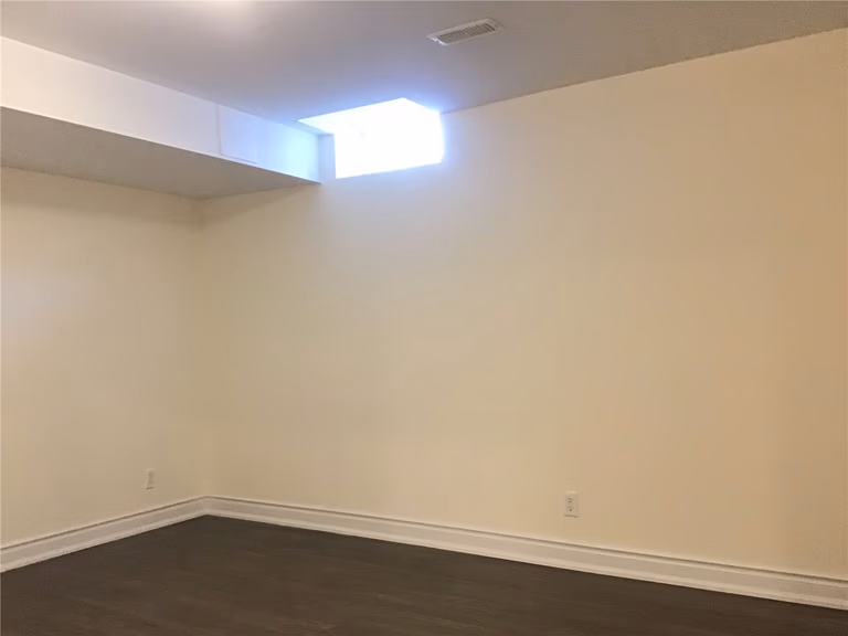 This Mississauga basement renovation features a clean and modern design with durable dark wood flooring, smooth painted walls, and a high-position window that allows natural light to brighten the space. The layout is simple yet functional, making it ideal for a future living area, home office, or rental suite.