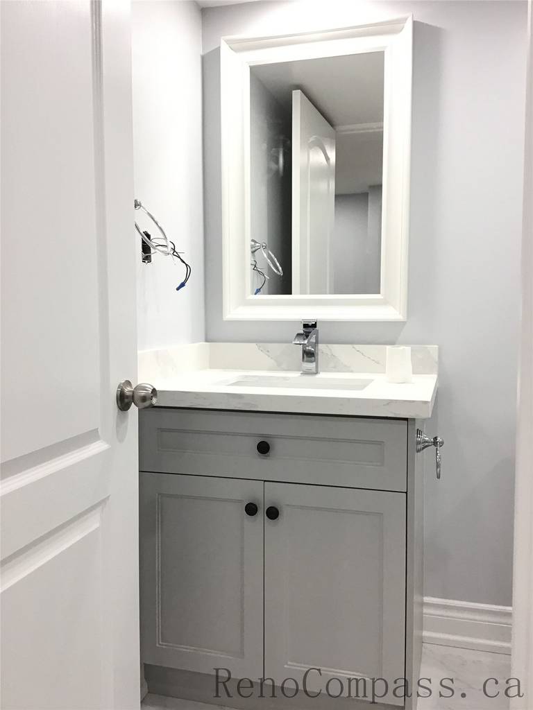 Newly renovated basement bathroom in Richmond Hill featuring a modern grey vanity cabinet, white quartz countertop, framed mirror, and sleek chrome faucet. Clean lines and neutral tones create a bright and functional space as part of a professional basement renovation project by a Toronto Renovation Company.