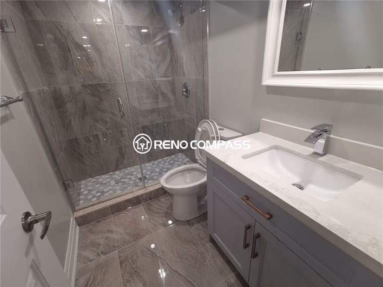 This Markham basement renovation showcases a fully upgraded bathroom featuring a glass-enclosed walk-in shower, marble-look porcelain tiles, modern vanity with quartz countertop, and sleek chrome fixtures. The combination of large-format floor tiles and detailed shower mosaic flooring enhances durability, water resistance, and visual appeal. A clean neutral color palette and contemporary finishes create a bright and functional basement bathroom environment. Completed by a professional Toronto renovation company, this project highlights expert tile installation, quality plumbing fixtures, and modern basement bathroom design tailored for homes in the Greater Toronto Area.