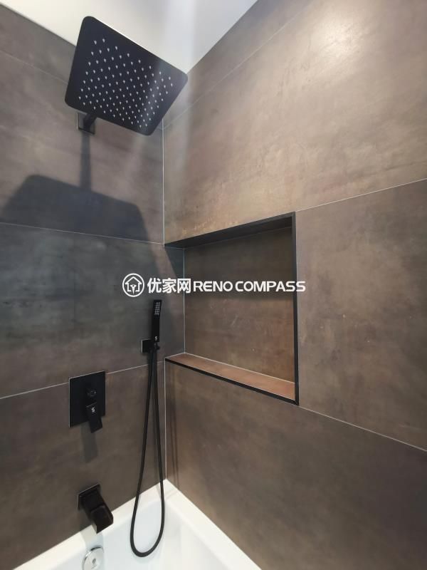 Walk-in shower detail from a North York interior renovation, featuring a ceiling-mounted rainfall showerhead, matte black fixtures, and a recessed wall niche for built-in storage. Large-format wall tiles create a seamless, low-maintenance surface while maintaining a modern, spa-inspired aesthetic. The clean layout and integrated detailing reflect a bathroom renovation completed by a Toronto renovation company focused on durability, functionality, and refined construction quality.