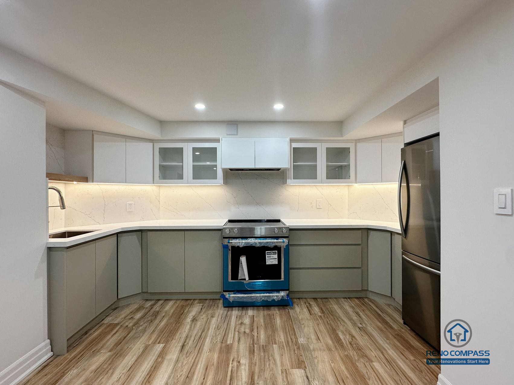 This image shows a completed basement kitchen renovation in Pickering, captured from a front-facing perspective to highlight the symmetrical layout and clean cabinet alignment. Custom cabinetry, integrated under-cabinet lighting, and a continuous countertop surface create a functional and visually balanced workspace. Neutral tones and consistent flooring help the kitchen blend seamlessly into the surrounding basement living area, supporting everyday use without visual clutter. Recessed ceiling lighting enhances brightness and clarity, reinforcing a practical, well-organized lower-level kitchen design.