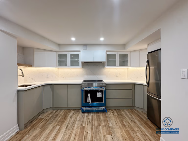 This image shows a completed basement kitchen renovation in Pickering, captured from a front-facing perspective to highlight the symmetrical layout and clean cabinet alignment. Custom cabinetry, integrated under-cabinet lighting, and a continuous countertop surface create a functional and visually balanced workspace. Neutral tones and consistent flooring help the kitchen blend seamlessly into the surrounding basement living area, supporting everyday use without visual clutter. Recessed ceiling lighting enhances brightness and clarity, reinforcing a practical, well-organized lower-level kitchen design.