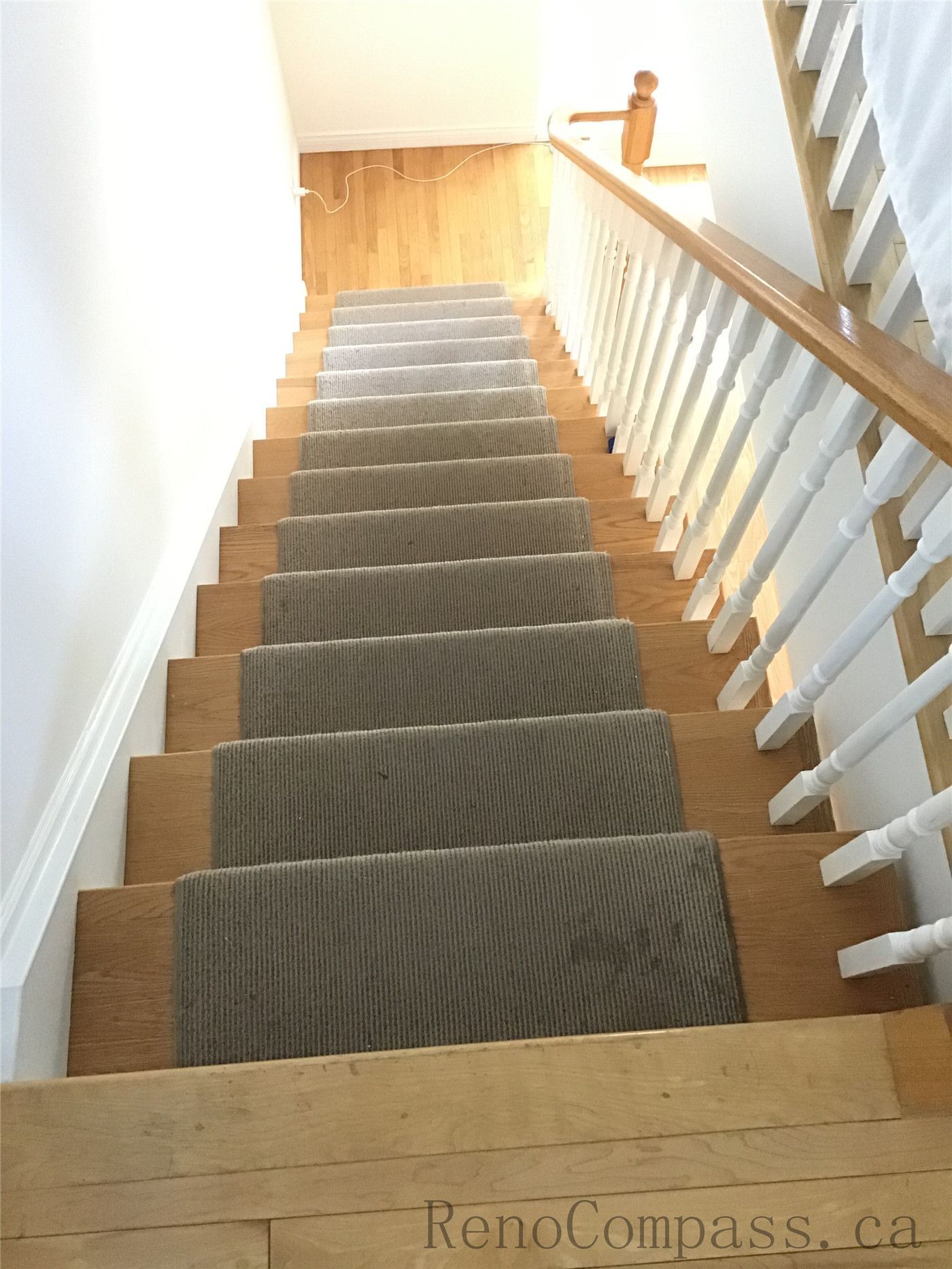 This image showcases a staircase renovation in Oakville featuring hardwood steps combined with a carpet runner for added comfort and safety. The clean white railings and smooth transition to the lower-level flooring highlight a well-integrated design that enhances both functionality and visual continuity.