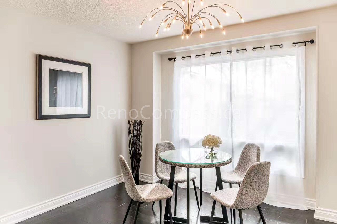 A bright dining area interior renovation in Toronto featuring a round glass dining table, modern pendant chandelier, and large window with sheer curtains for natural light. The space emphasizes comfort, balance, and everyday functionality, reflecting thoughtful Toronto interior renovation and interior design craftsmanship.