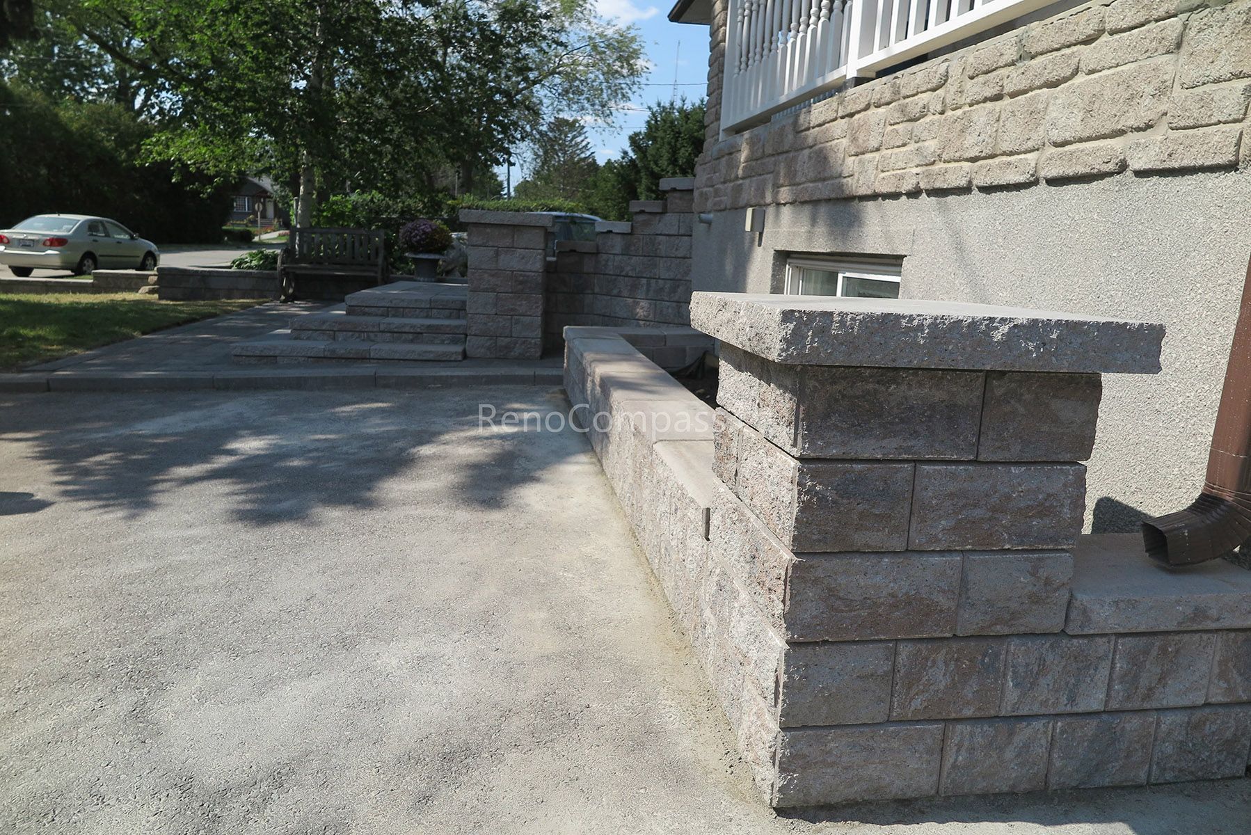 This close-up view highlights the precision craftsmanship of the stone retaining wall and interlocking patio installation in Mississauga. The textured concrete blocks and smooth stone cap provide structural stability while delivering a clean, layered aesthetic. Integrated seamlessly with the surrounding landscaping and planting design, this hardscape feature enhances both durability and visual depth. Professionally completed by Reno Compass Inc., this project reflects expert workmanship in outdoor interlocking and landscape construction.