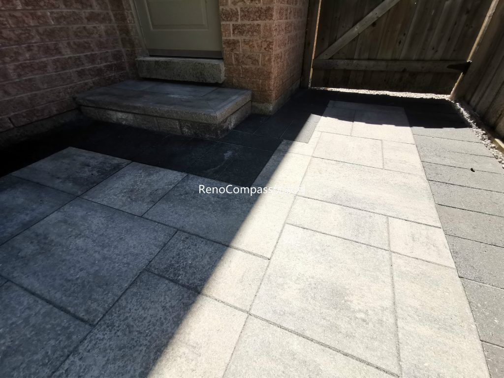 Modern Mississauga backyard patio featuring interlocking stone flooring, raised retaining wall, and landscaped garden beds, creating a functional and elegant outdoor living space.