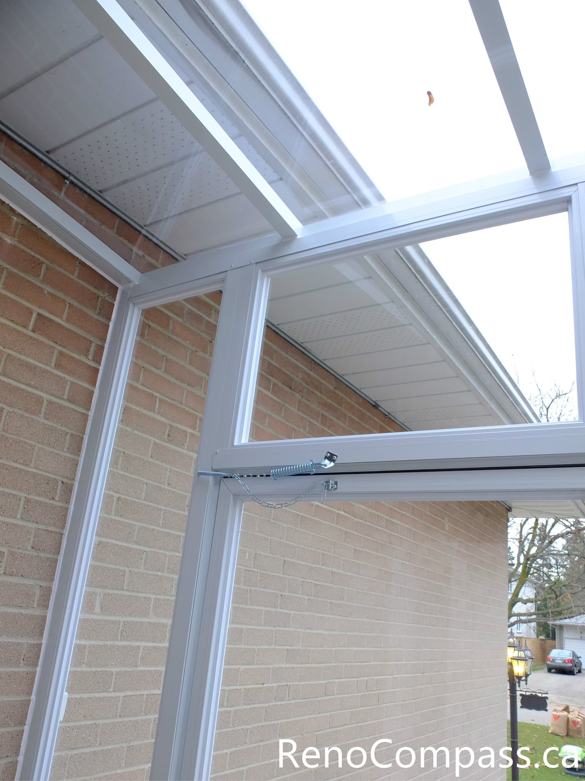 This close-up image highlights the hinge and support mechanism of a custom glass storm door installed at a North York home entrance. The reinforced metal hinge, spring support, and secure frame structure ensure smooth operation and long-term durability while protecting the main entrance from wind, snow, and rain. The white aluminum frame and transparent glass panels create a clean and modern entry vestibule design. Installed by a professional Toronto renovation team, this storm door system improves both functionality and weather protection for the home entrance.