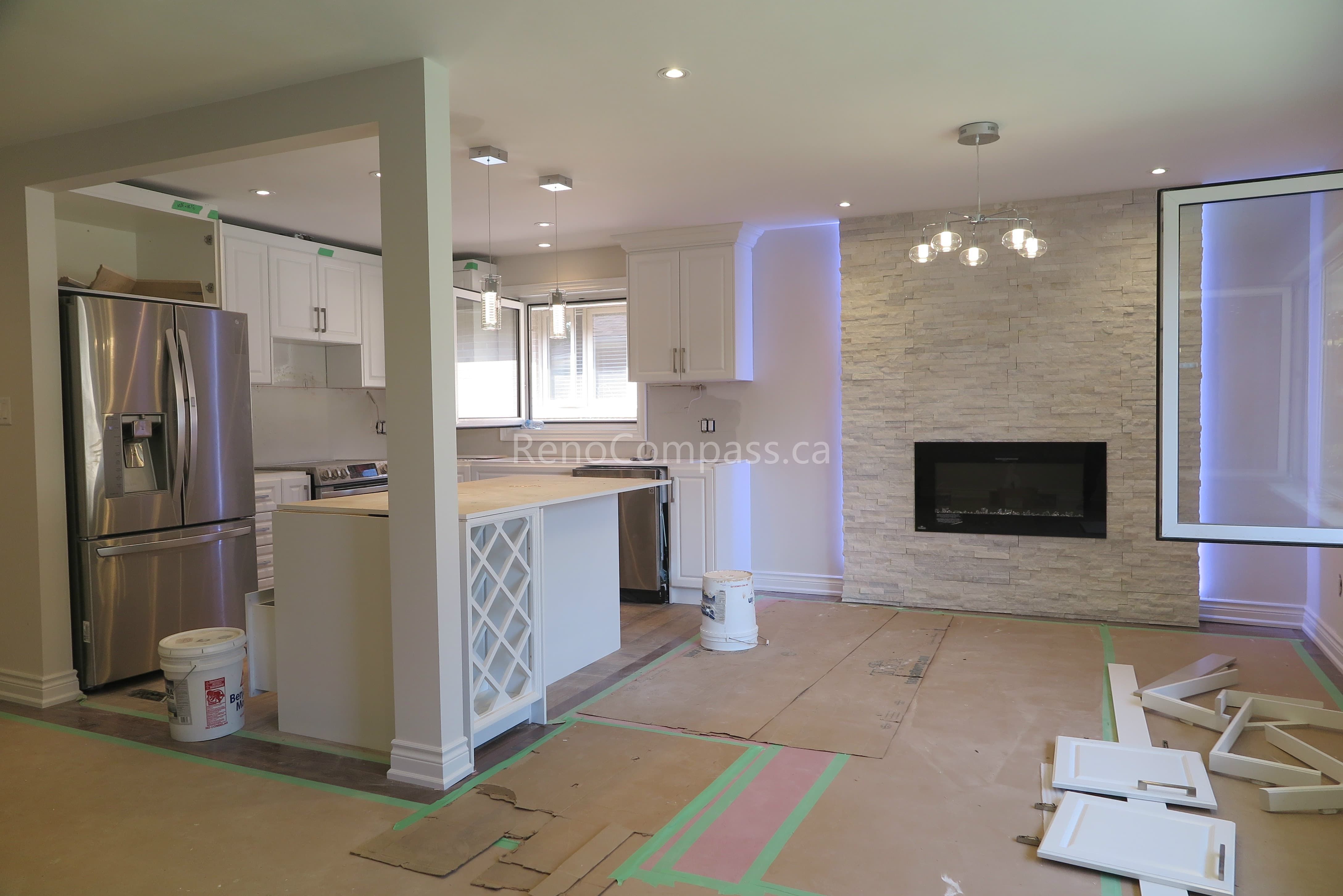 Open-concept kitchen and living area during a North York interior renovation project, featuring custom white cabinetry, kitchen island, recessed lighting, and a modern fireplace feature wall. This renovation is completed by a professional Toronto renovation company, focusing on space optimization, modern design, and high-quality interior finishes.