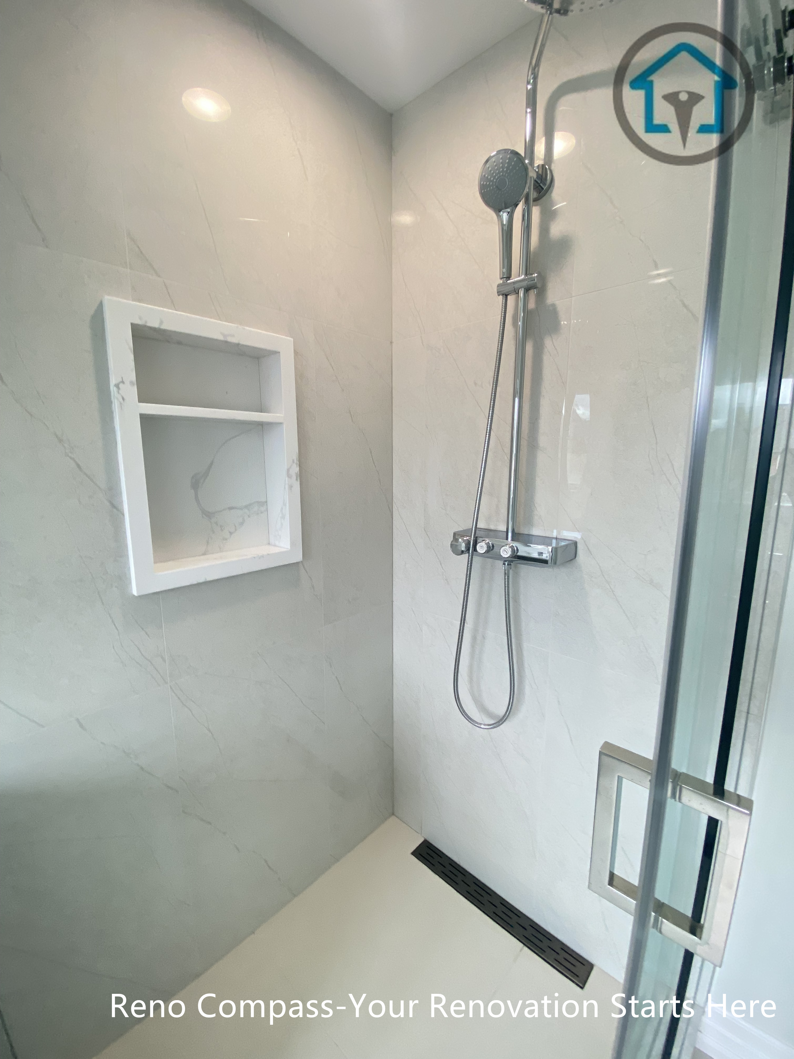 This curbless walk-in shower is designed for both functionality and visual clarity. Large-format light porcelain tiles create a seamless look, while the recessed wall niche provides practical storage without interrupting the clean lines. A linear floor drain and frameless glass enclosure enhance accessibility and reinforce the modern, minimalist design.