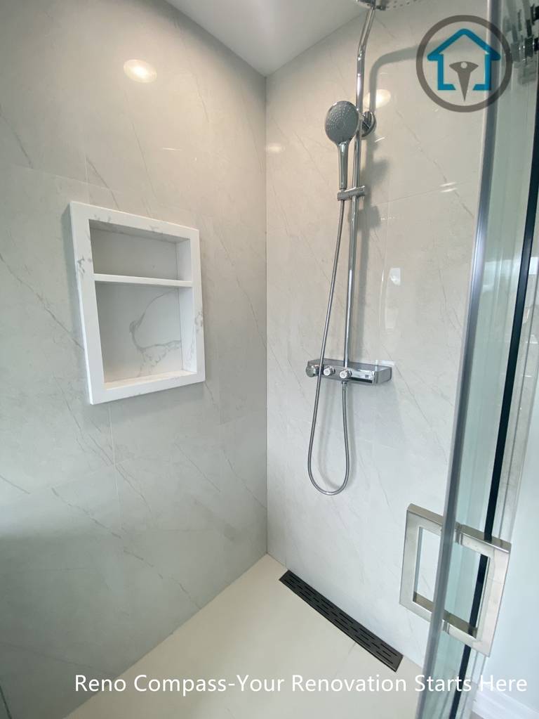 This curbless walk-in shower is designed for both functionality and visual clarity. Large-format light porcelain tiles create a seamless look, while the recessed wall niche provides practical storage without interrupting the clean lines. A linear floor drain and frameless glass enclosure enhance accessibility and reinforce the modern, minimalist design.