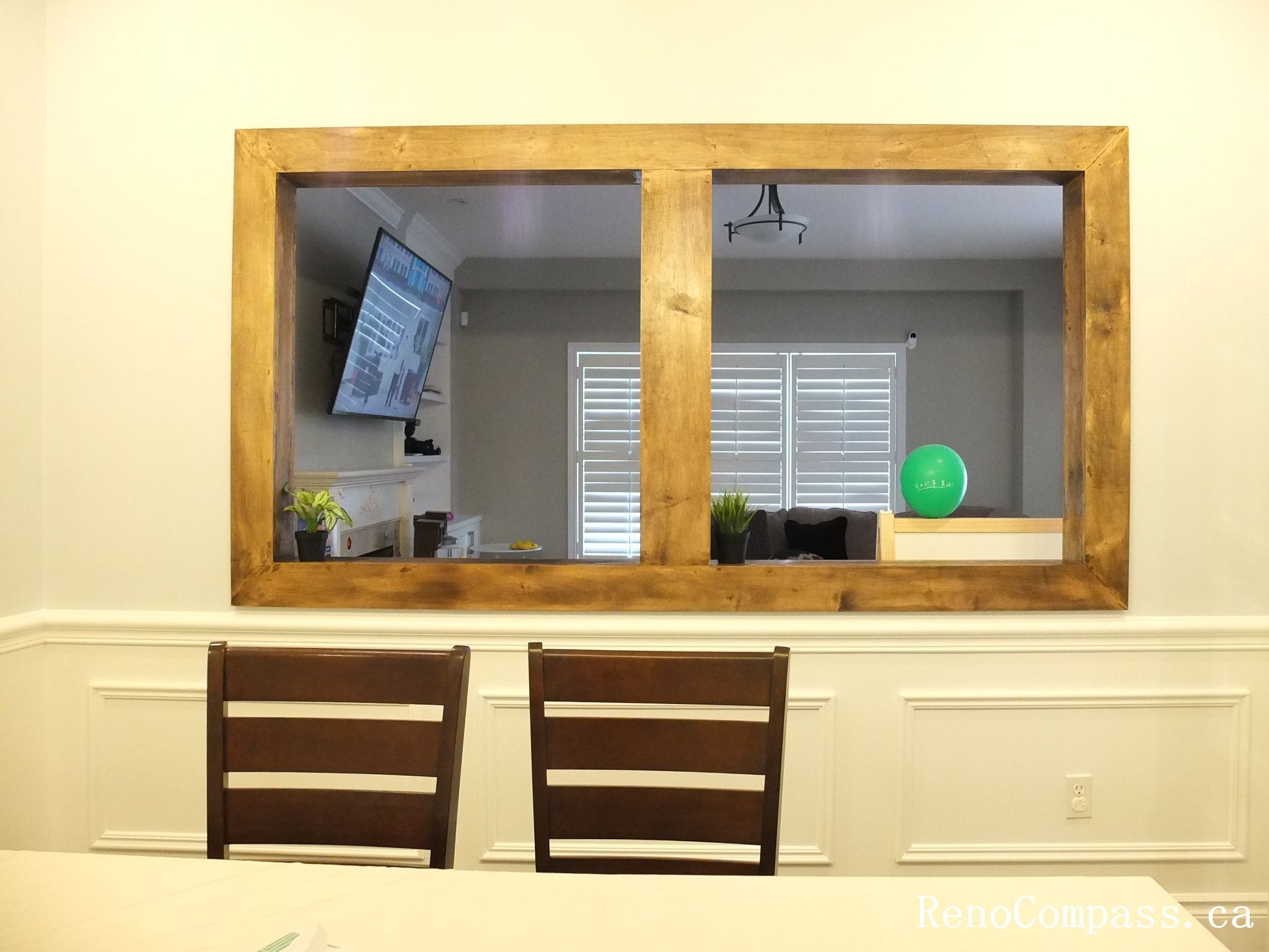 This Newmarket interior renovation highlights a bright and elegant dining room designed for both everyday meals and family gatherings. The space features classic wall wainscoting, dark hardwood flooring, and a modern rectangular pendant light fixture that adds a contemporary touch above the dining table. A large interior window opening with a warm wood frame connects the dining area to the adjacent living space, creating a more open and interactive layout. Completed by Reno Compass Inc., this project demonstrates thoughtful interior design and quality craftsmanship for modern family homes.