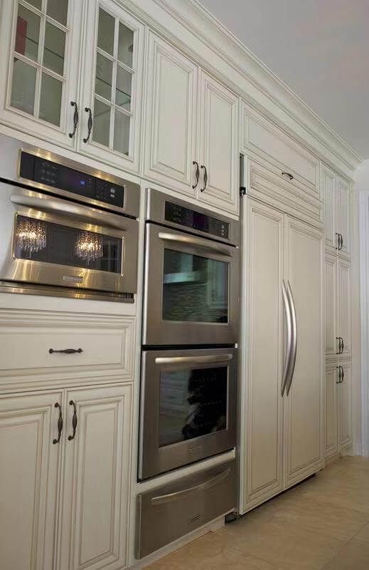 This European-style kitchen renovation showcases elegant custom white cabinetry with detailed panel molding and classic hardware, creating a refined and timeless aesthetic. The kitchen features a fully integrated built-in refrigerator and double wall ovens, maximizing functionality while maintaining a seamless design.

The large central island is finished with a dark natural stone countertop, adding contrast and sophistication to the space. Crystal chandeliers enhance the luxurious European atmosphere, combining traditional charm with modern convenience.

This kitchen design is ideal for homeowners seeking a high-end, classic European kitchen upgrade with enhanced storage, premium finishes, and a cohesive layout.