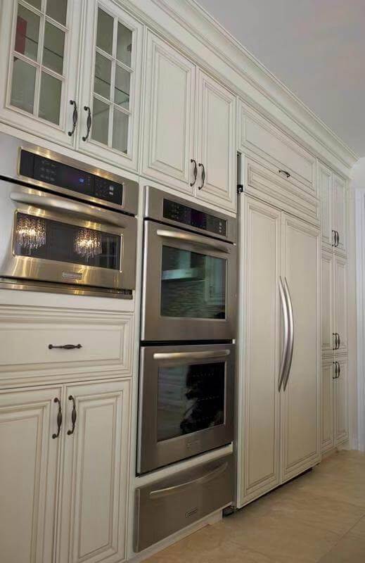 This European-style kitchen renovation showcases elegant custom white cabinetry with detailed panel molding and classic hardware, creating a refined and timeless aesthetic. The kitchen features a fully integrated built-in refrigerator and double wall ovens, maximizing functionality while maintaining a seamless design.

The large central island is finished with a dark natural stone countertop, adding contrast and sophistication to the space. Crystal chandeliers enhance the luxurious European atmosphere, combining traditional charm with modern convenience.

This kitchen design is ideal for homeowners seeking a high-end, classic European kitchen upgrade with enhanced storage, premium finishes, and a cohesive layout.