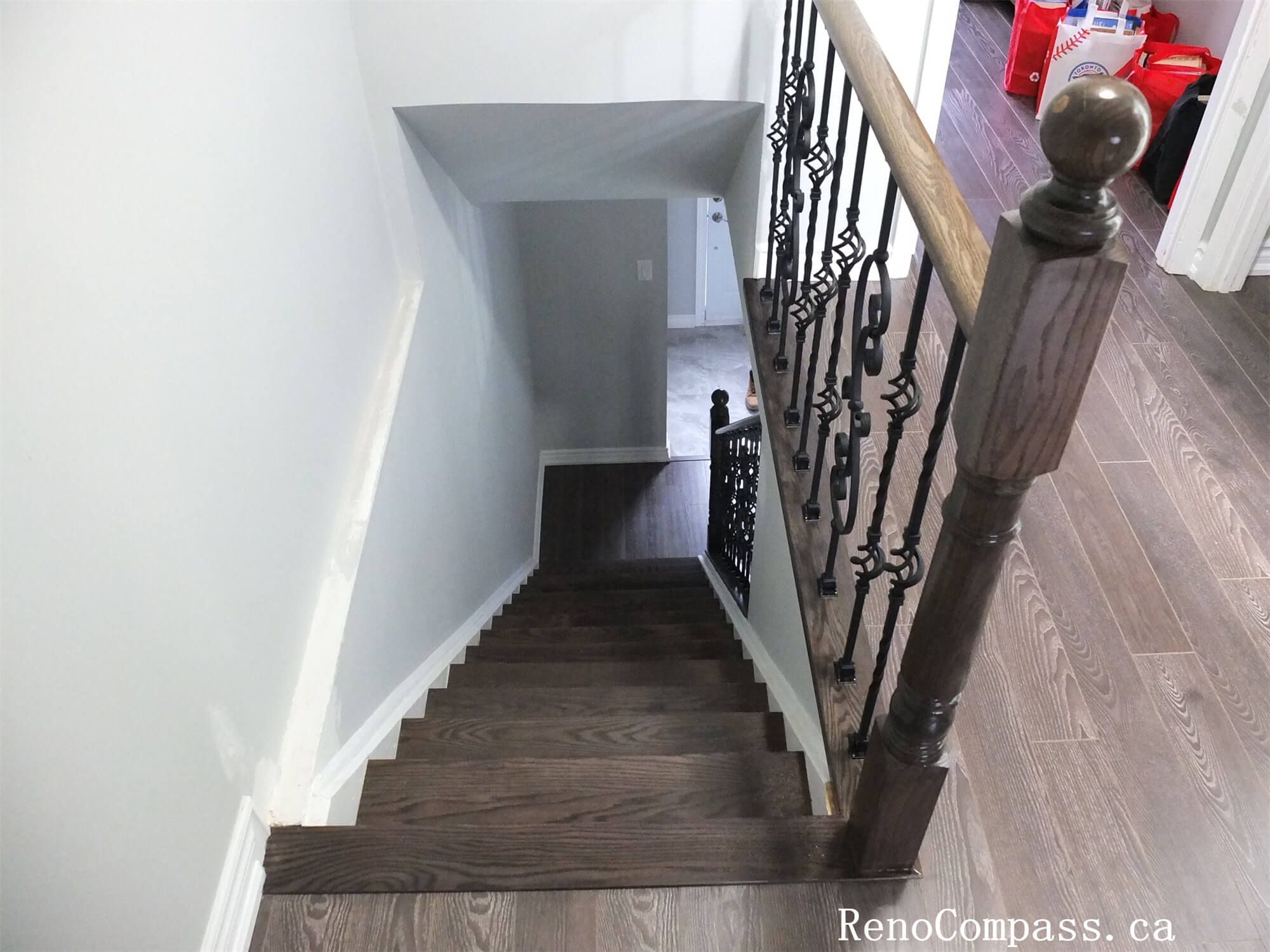 This North York interior renovation showcases a downward view of the staircase featuring dark wood steps, matching landing flooring, and decorative iron balusters. The continuous material transition between the stair treads and upper-level flooring enhances visual flow and durability, while the clean railing design improves safety and elegance in this Toronto home renovation project.