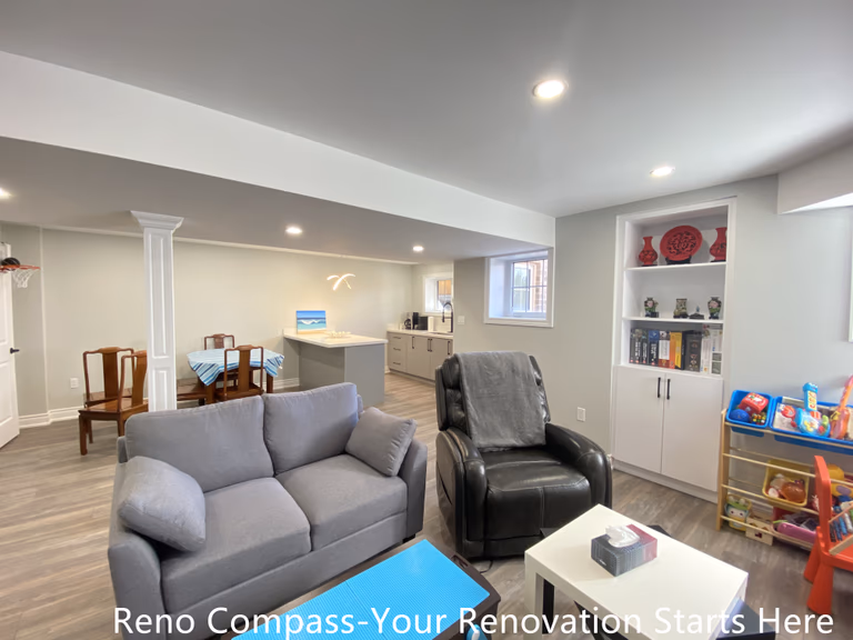 Open-concept basement renovation in Oakville featuring a spacious family living area with recessed lighting, structural columns, vinyl plank flooring, built-in shelving, and seamless connection to a custom bar area, creating a bright and functional multi-purpose basement space, completed by Reno Compass Inc.